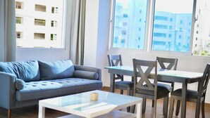 A modern living room with a grey sofa, a glass coffee table, and a dining table with chairs. - Estudio apartamento Juan Dolio (Guayacanes)