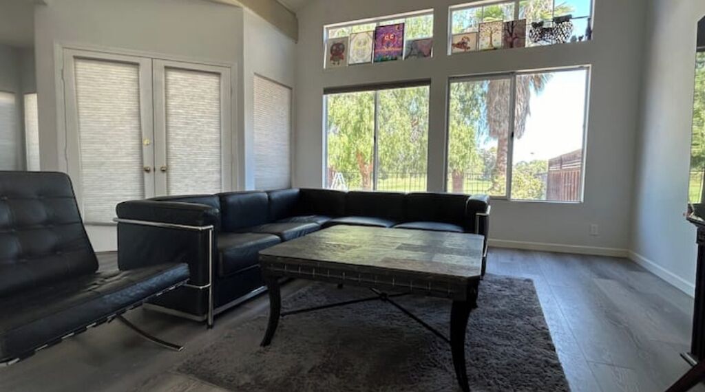 A living room with a sectional sofa, a coffee table, and a large window with blinds.