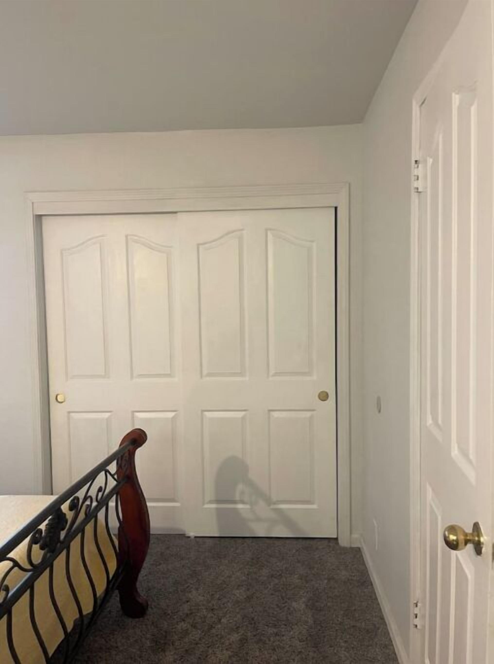 Una habitación con una puerta blanca cerrada, una silla de madera con estructura metálica y piso alfombrado.