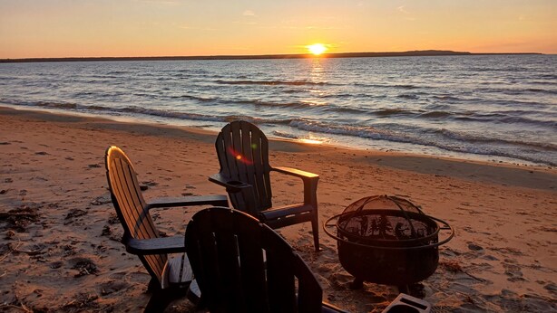 A beach with two Adirondack chairs facing the ocean at sunset. - Rustic Moose Lakefront Guest Cabin on the Shore of Lake Superior (Brimley)