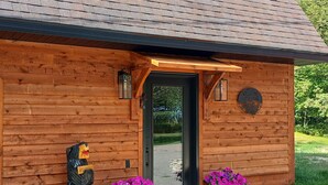 A wooden cabin with a black door, a welcome sign, and two flower pots. - Rustic Moose Lakefront Guest Cabin on the Shore of Lake Superior (Brimley)