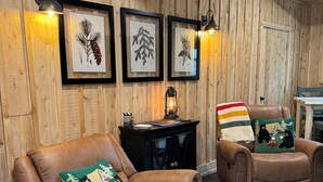 A cozy room with wooden walls, two leather recliners, a small table, and framed botanical prints. - Rustic Moose Lakefront Guest Cabin on the Shore of Lake Superior (Brimley)