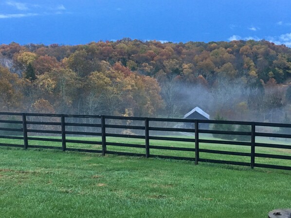 A rural landscape with a wooden fence, green grass, and a hill of trees in autumn colors. - View on the Ridge close to Ark Encounter. (Williamstown)