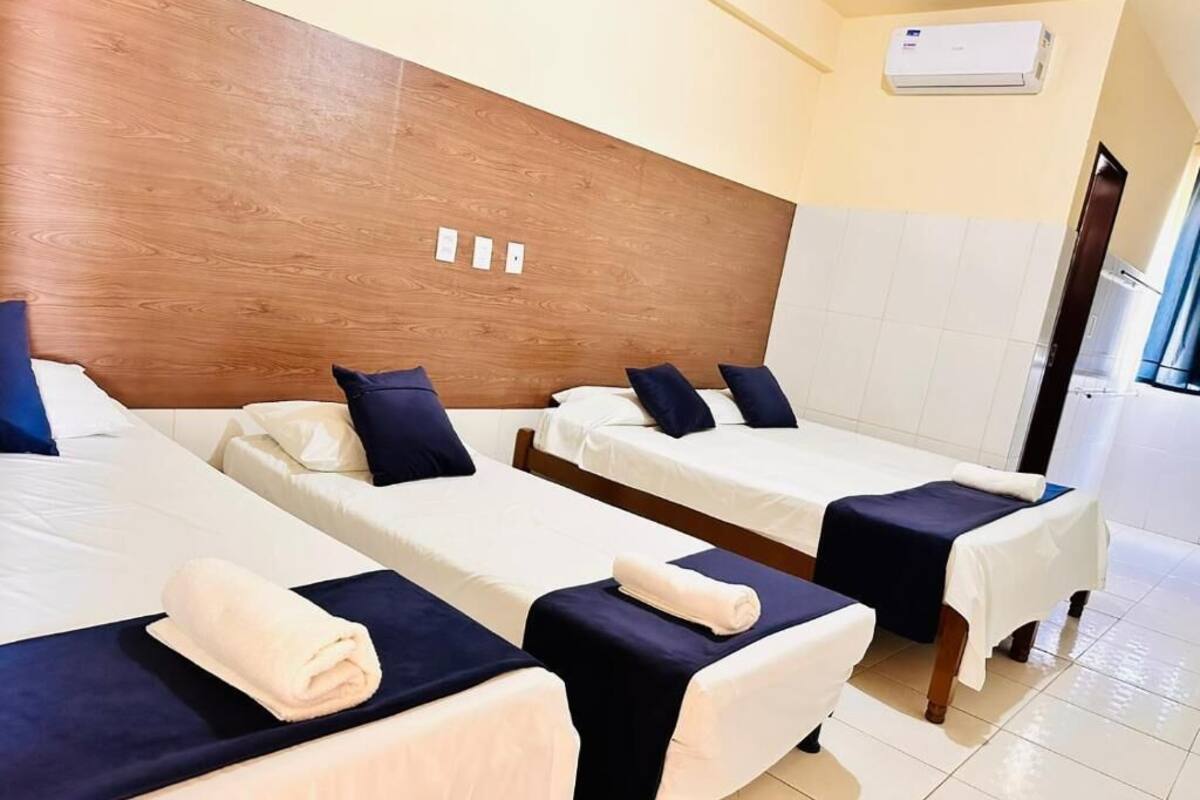 A hotel room with three single beds, each with a white mattress and dark blue headboard.