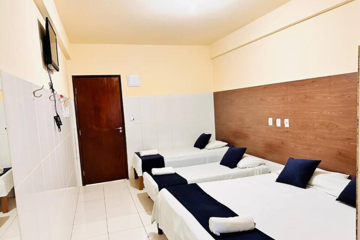 A hotel room with three single beds, a wooden headboard, a TV mounted on the wall, and a door with a handle.
