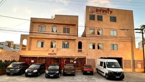 A building with the name 'Infinity Pousada' on the facade. There are several cars parked in front, and a white van is visible inside. - INFINITY POUSADA (Aracaju)