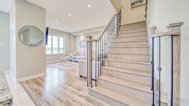 A spacious living area with a wooden staircase, a round mirror on the wall, and a large window providing natural light.