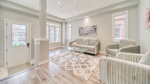 A spacious living room with a beige sofa, a glass coffee table, and a patterned rug.