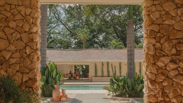 A stone archway leading to a pool area with a tiled roof and cacti.