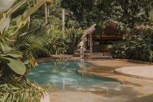 Un área de piscina con diseño curvo, rodeada de exuberante vegetación y una zona de bar con asientos.
