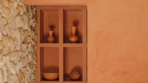 Une pièce avec un mur en pierre, un meuble en bois contenant de la poterie, et un petit chien.