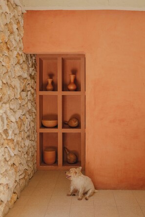 Una habitación con pared de piedra, un mueble de madera con cerámica y un perro pequeño.