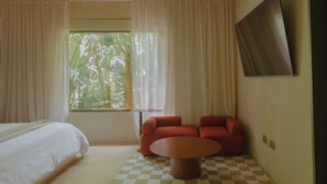 Une chambre d’hôtel avec un lit, un sol à carreaux, un canapé rouge, une petite table et une fenêtre avec des rideaux.