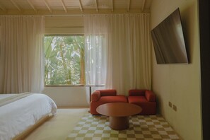 Una habitación de hotel con una cama, suelo de cuadros, un sofá rojo, una mesita y una ventana con cortinas.