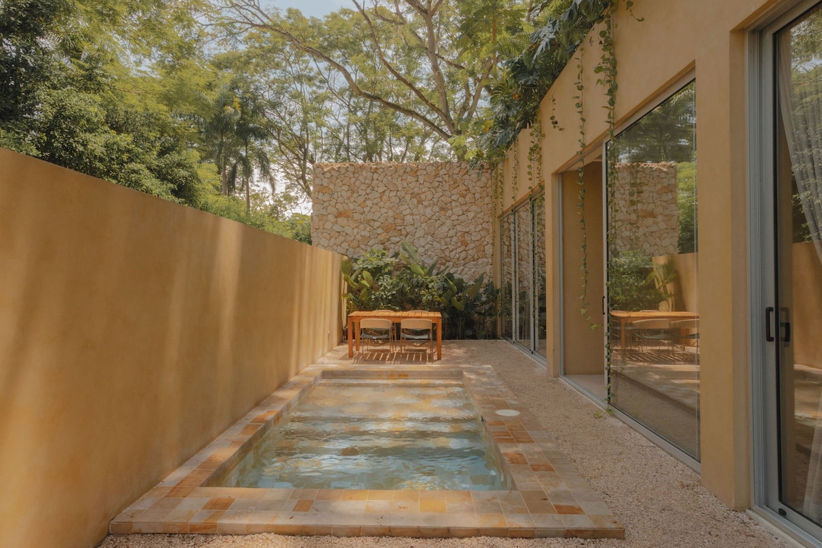 A swimming pool with a stone wall and a table with chairs in a covered outdoor area.