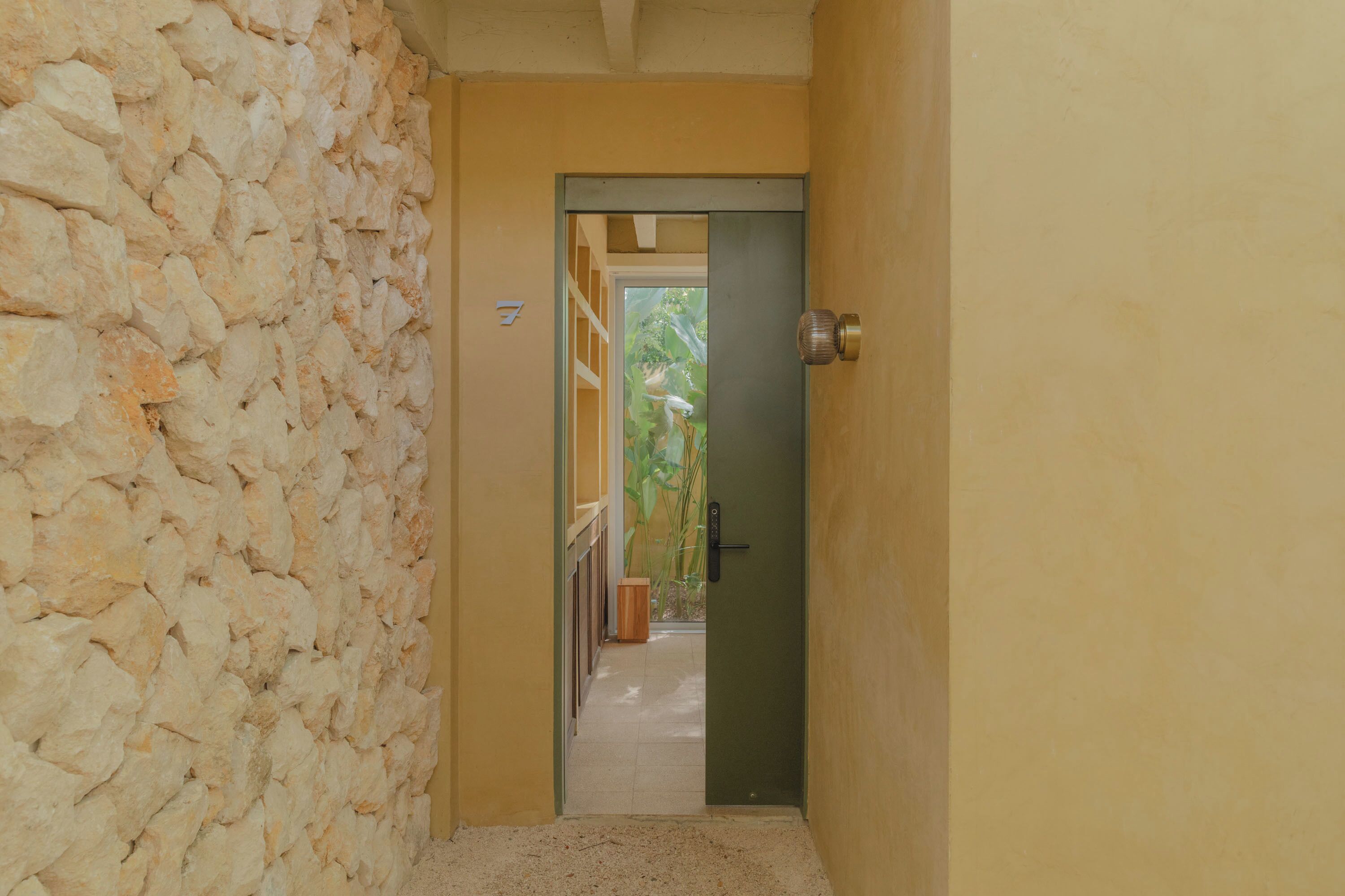 Un couloir avec un mur en pierre d’un côté et une porte dotée d’un cadre vert donnant sur un balcon.