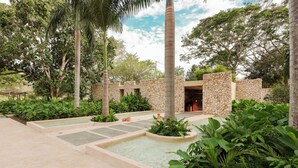 Un patio con pared de piedra, fuente de agua y abundante vegetación.