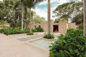 Un patio con pared de piedra, fuente de agua y abundante vegetación.