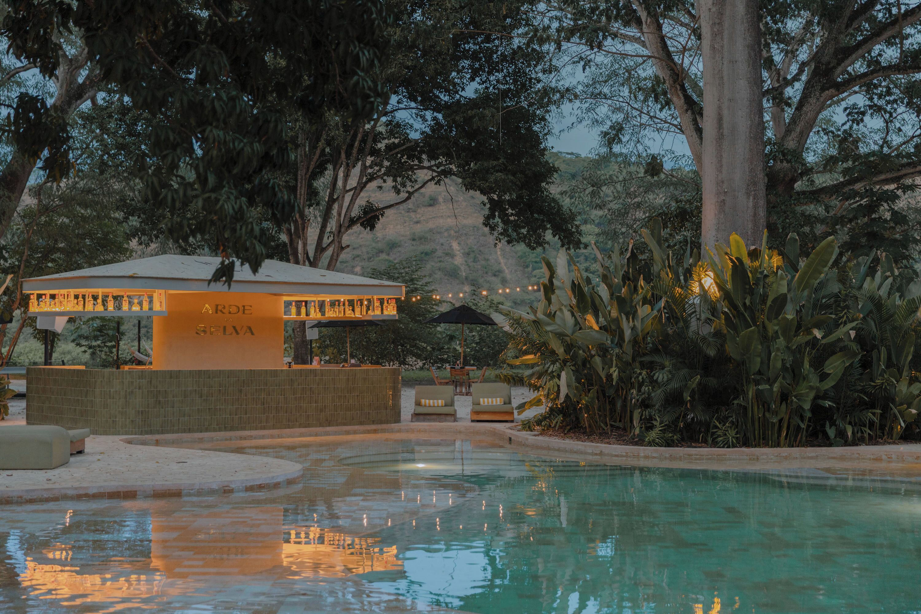 A pool area with a bar named 'ARDE LA SELVA' and surrounding tropical vegetation.