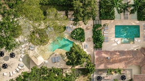 Vista aérea de un resort con piscina central, tumbonas y zona de patio con baldosas.