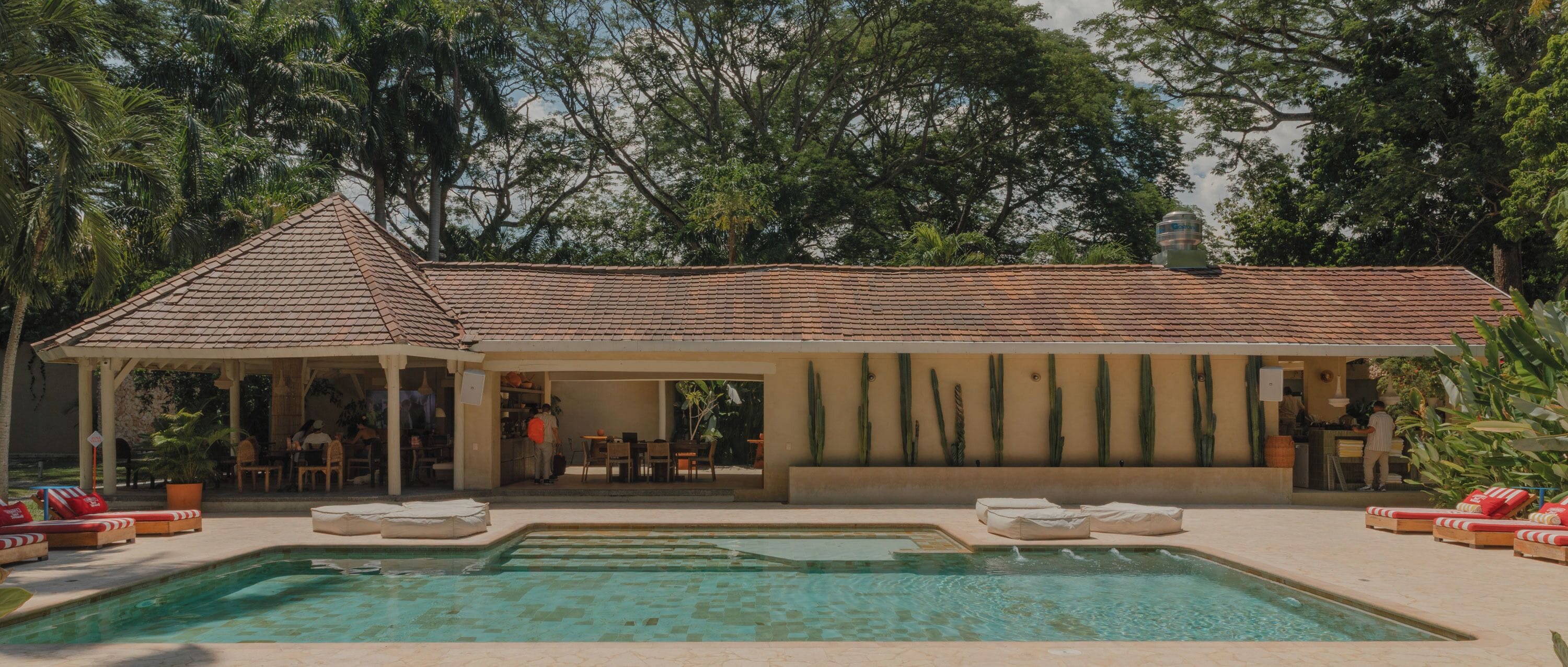 A poolside area with a covered seating area, a pool, and a view of the surrounding trees.