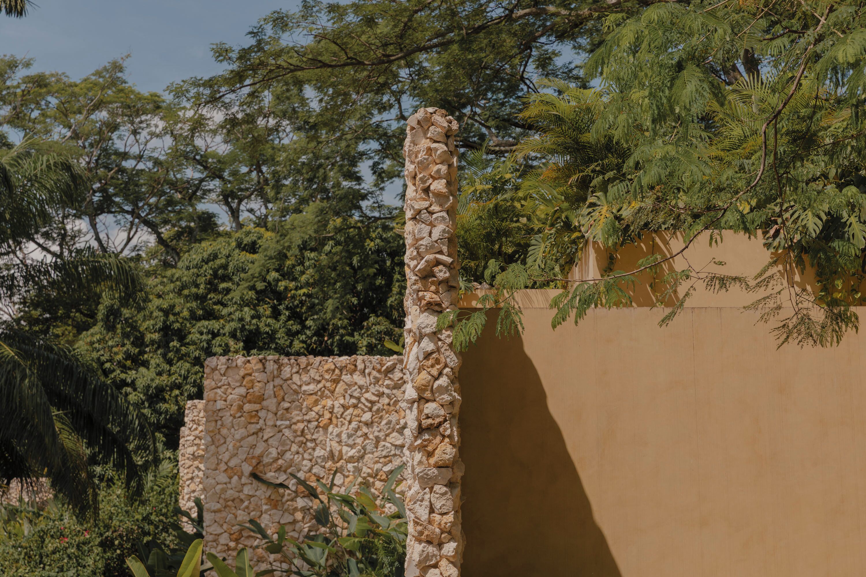 A stone wall with a textured surface, surrounded by lush greenery and trees.