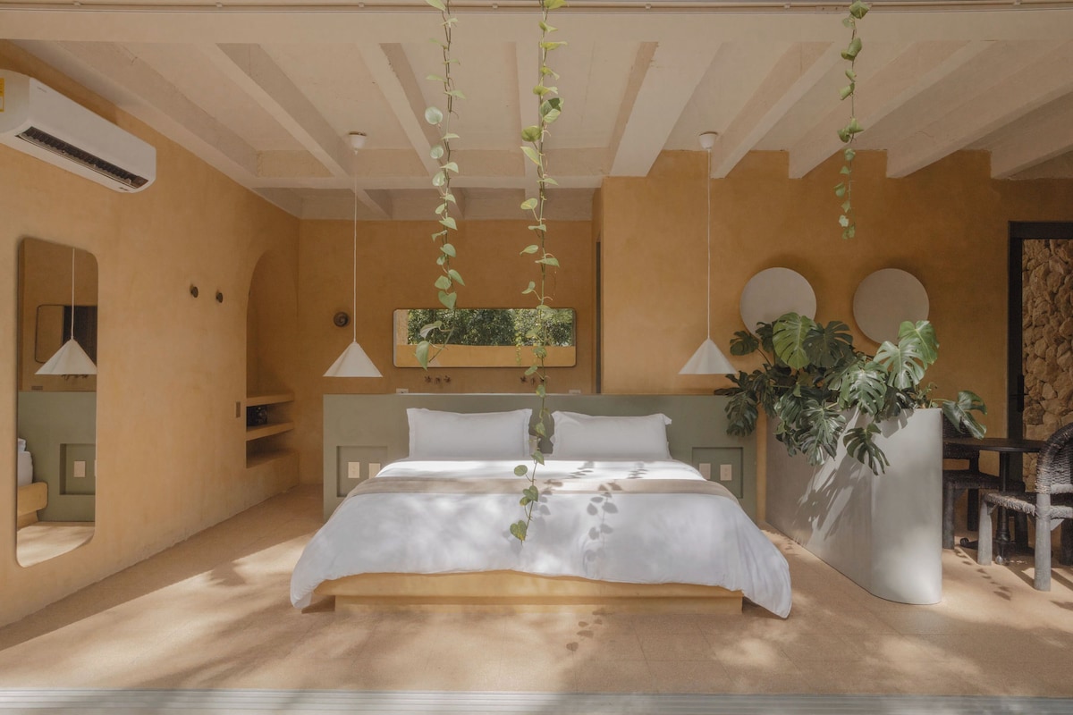 A bedroom with a bed, bedside tables, a mirror, a hanging plant, and a potted plant.