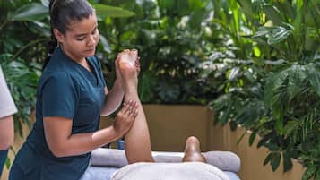 A person receiving a foot massage in a room with a massage table, a towel, and green plants in the background.