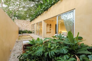 Un patio exterior moderno con pared de piedra, una pequeña fuente de agua y abundante vegetación.
