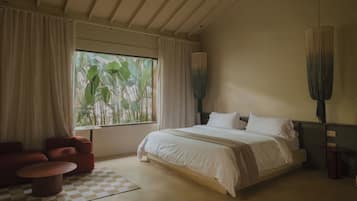 Een slaapkamer met een groot bed, een stoel, een geruit kleed en een raam met gordijnen.