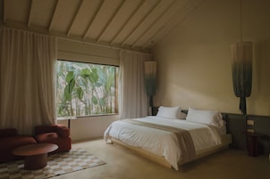 A bedroom with a large bed, a chair, a checkered rug, and a window with curtains.