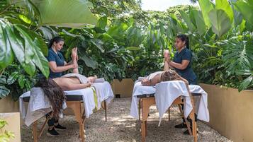 A spa area with two massage tables, one occupied by a person receiving a massage, and another with a person preparing to give a massage.
