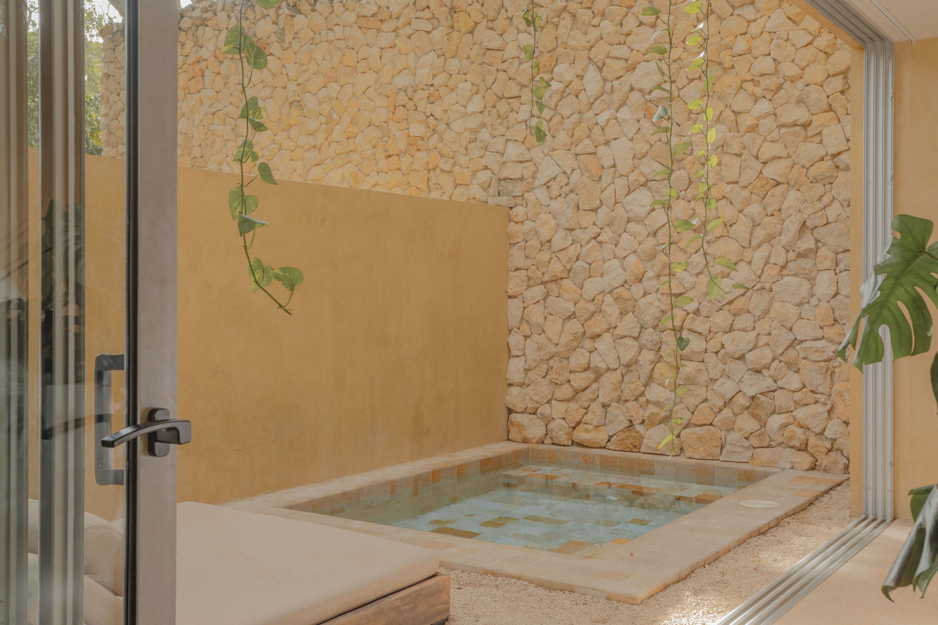 A spa room with a stone wall, a glass door, and a small pool.