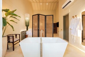 Ein modernes Badezimmer mit einer großen Badewanne, einem Holzstuhl, einer Topfpflanze und einem Raumteiler.