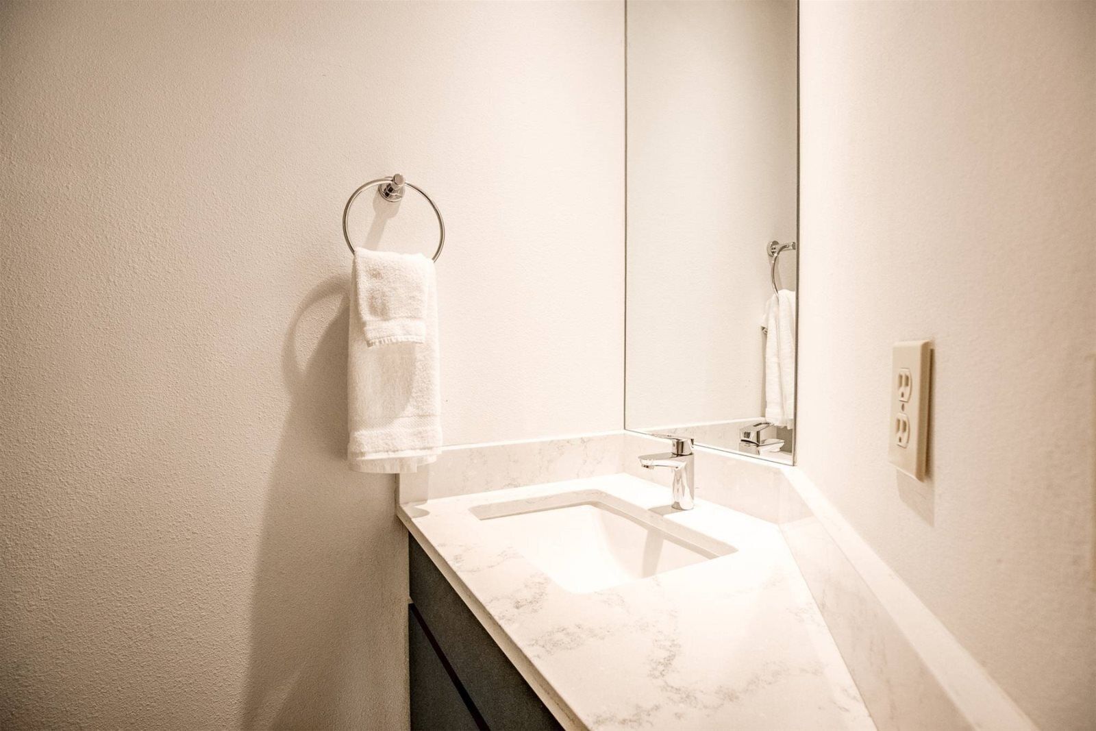 Un baño con lavamanos de mármol, toallero y espejo.