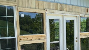 A building with large windows and a door, wooden deck, and gravel ground. - Cabin with Character (New Lexington)