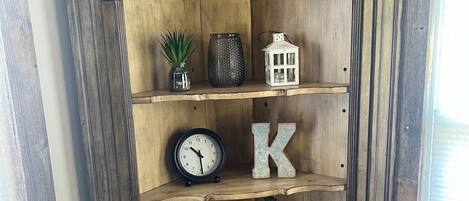 A wooden cabinet with shelves containing a clock, a candle, decorative items, and a letter 'K'.