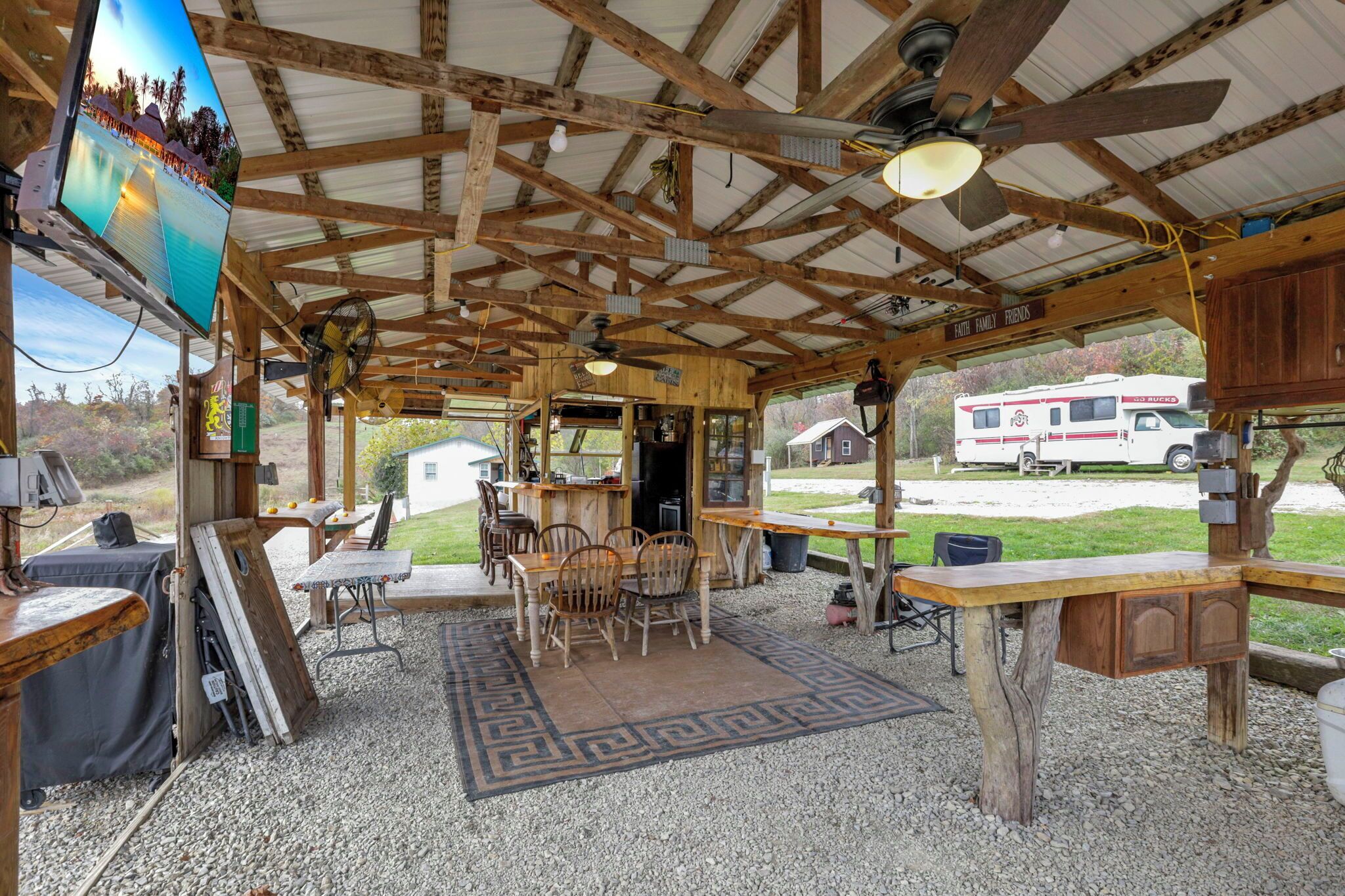 Een rustiek RV-park met houten gebouwen, een eethoek en uitzicht op een witte RV op de achtergrond.