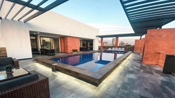 Un espace piscine extérieur moderne doté d’une piscine rectangulaire, de chaises longues et d’un patio couvert.