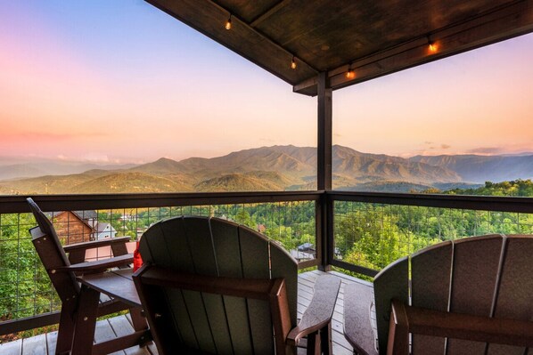 Un balcón con dos sillas Adirondack y una mesa, con vistas a un paisaje montañoso.