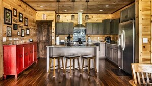 A rustic kitchen with wooden walls, a central island with stools, and modern appliances. - VIEWS/YARD/Hot Tub/Theater/Game Room - Wild Ginger (Gatlinburg)