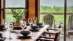 A dining table set with bowls and wine glasses, a potted plant, and a view of mountains through large windows. - VIEWS/YARD/Hot Tub/Theater/Game Room - Wild Ginger (Gatlinburg)
