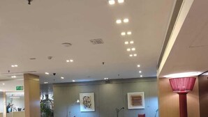 Un hall d’entrée spacieux avec un sol en marbre, un coin salon avec des canapés et des tables, et un lampadaire rouge.