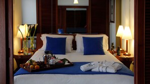 Une chambre d’hôtel avec un grand lit, deux oreillers bleus, un plateau avec des fruits et une machine à café, ainsi que deux lampes de chevet.