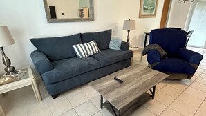 A living room with a dark blue sofa, a striped pillow, a wooden coffee table, a lamp, and a blue armchair.