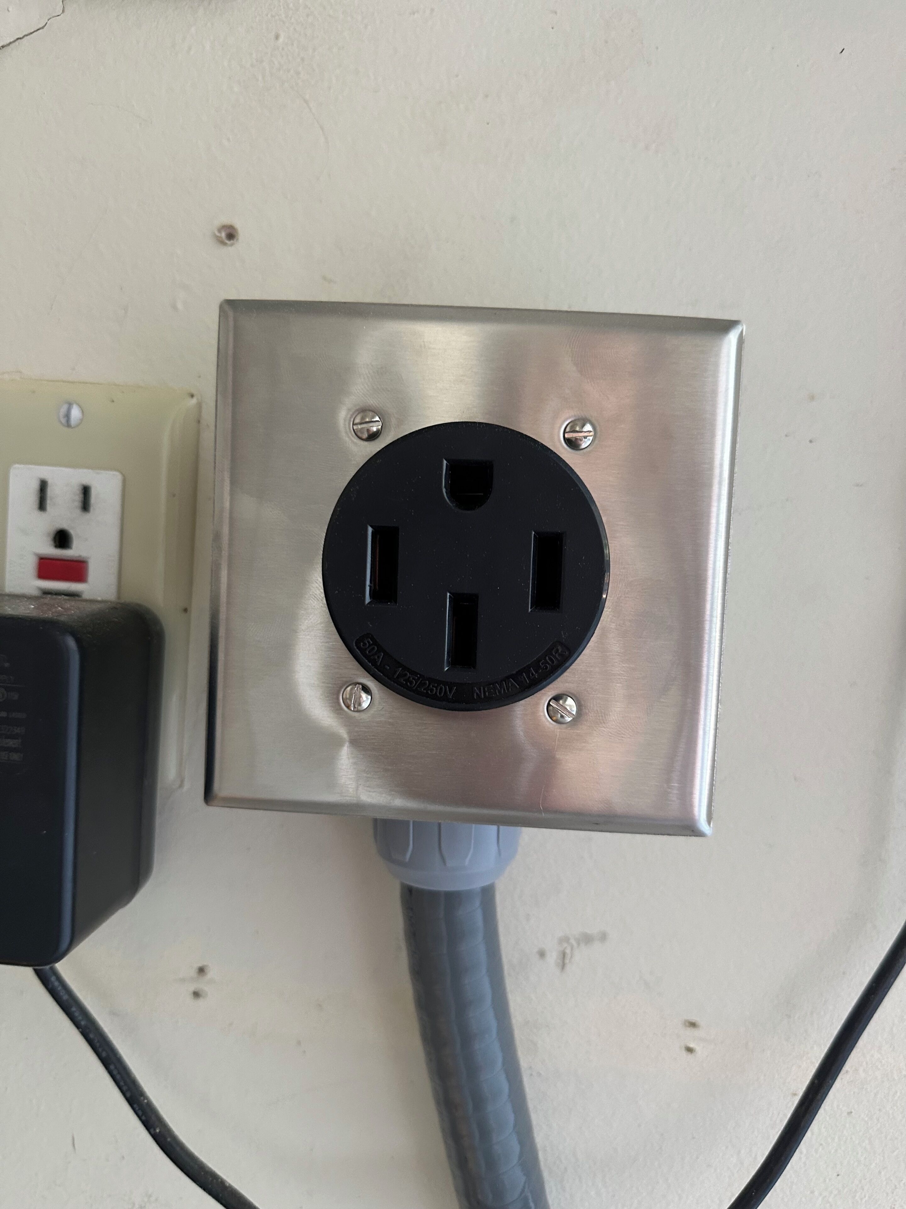A metallic electrical outlet with a plug inserted, a wall socket with a red switch, and a cable connected to the outlet.