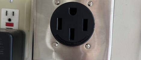 A metallic electrical outlet with a plug inserted, a wall socket with a red switch, and a cable connected to the outlet.