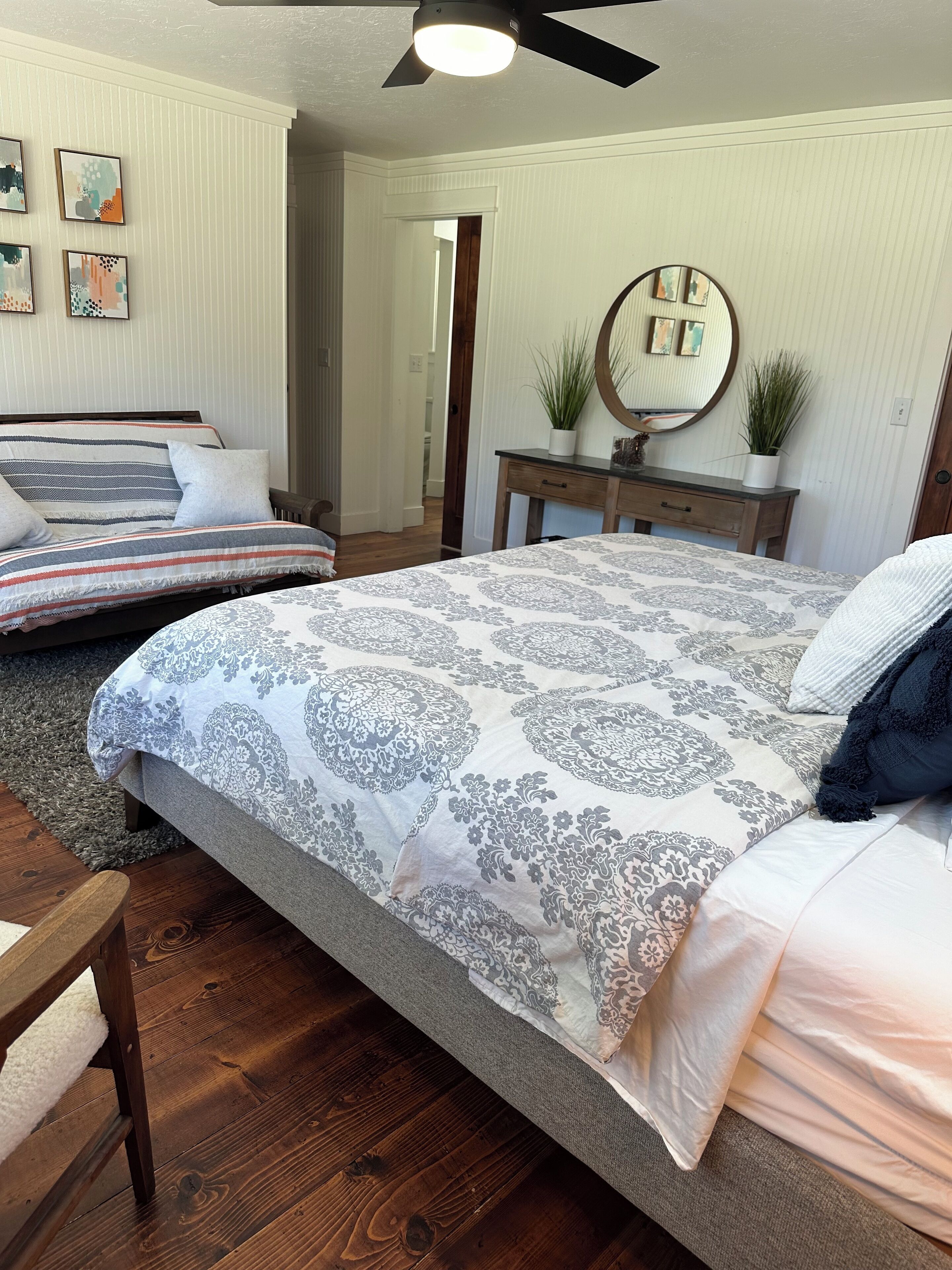 A bedroom with a large bed, a bedside table with a mirror, and a wooden dresser.
