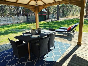 Un espace extérieur abrité, aménagé pour prendre les repas, avec une table et des chaises, un tapis à motifs bleus et une terrasse en bois.