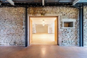 A stone-walled hallway leading to a room with a wooden door, a stone fireplace, and a hanging light fixture.